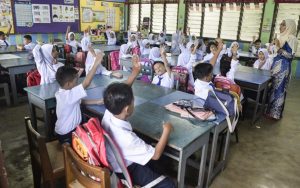 Malaysian students raising their hands up in front of their teacher